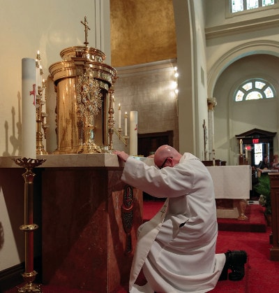 A priest kneeling before the Blessed Sacrement